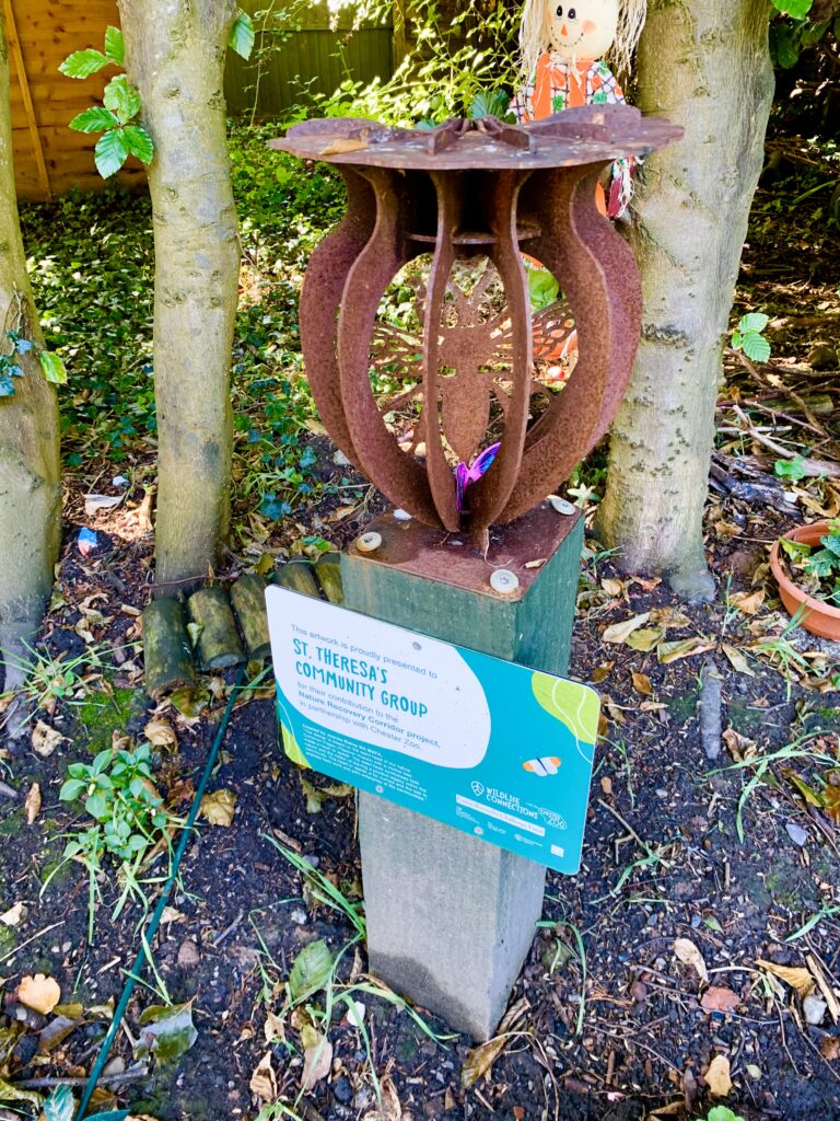 Cor-ten steel sculpture of a bee inside half section of a poppy seed head.